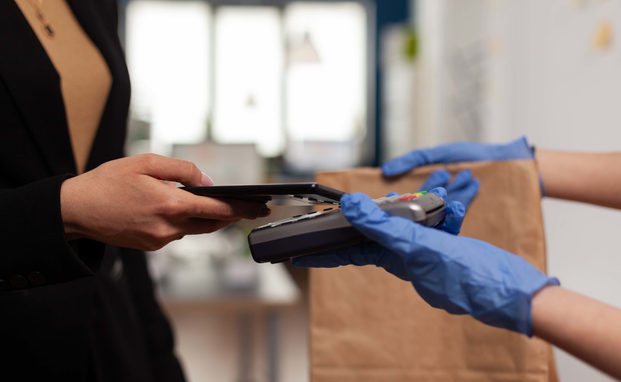 Delivery guy wearing protective gloves receiving paymant from businesswoman